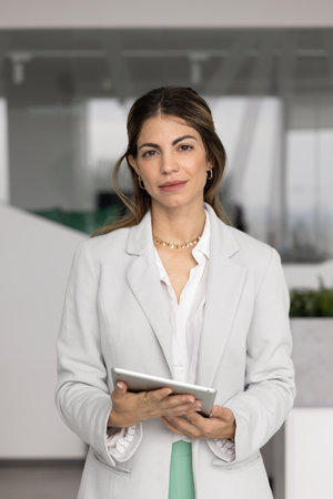 Portrait of serious businesswoman holding digital tablet looking at camera exuding confidence,...