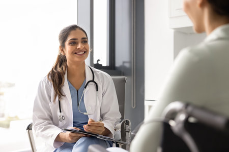 Happy young Indian rehabilitation doctor in white coat giving consultation, medical advice to...