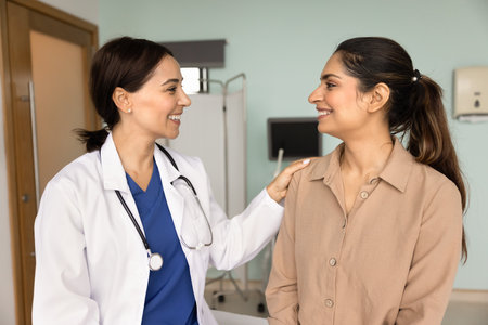 Positive empathetic doctor touching shoulder of happy patient in medical exam room, talking, smiling, discussing therapy, giving motivation for treatment, support, comfortの写真素材
