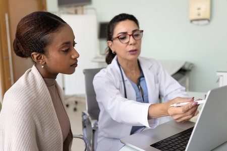 Elderly female doctor showing medical information to woman patient on laptop, providing lab test results, explaining diagnosis or X-ray, MRI scans, giving medical consultation about treatment optionsの写真素材