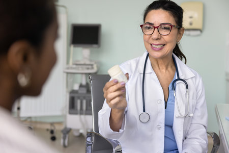 Older female doctor showing pills bottle to woman patient, prescribing vitamins, food supplement, innovative painkiller, prescribe antibiotics after medical check-up, recommending effective treatmentの写真素材