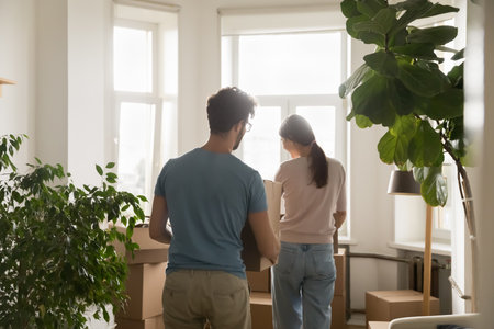 Arriving to new home. Rear view millennial husband wife walk with carton boxes in hands carry belongings to new flat apartment after renting purchasing prepare to unpack stuff on moving relocation dayの写真素材