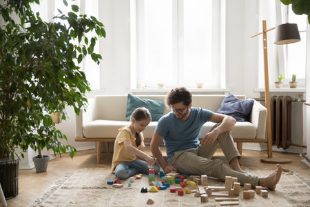 Learning through playing. Smiling father play with little daughter in cozy living room teach to build colorful constructions using toy wooden blocks share ideas help to develop imagination creativityの写真素材