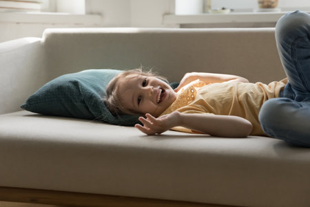 Peaceful fun and home relax. Portrait cute early school age girl lying on large comfy couch at living room with head on pillow look at camera with joyful happy laughter rest alone in safe warm spaceの写真素材