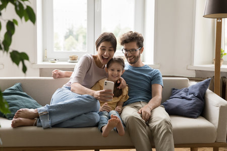 Great digital surprise. Overjoyed shocked family mom dad small daughter hug on couch scream wow...