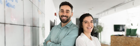 Wide image of two happy Latin team members posing in office, looking at camera, feels satisfied with...