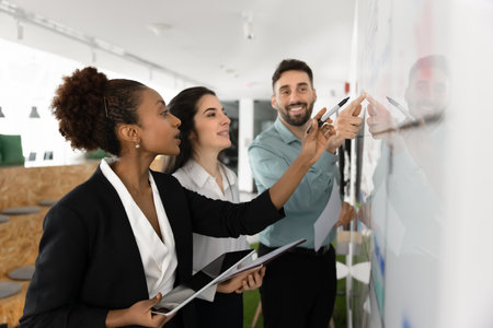 Diverse teammates brainstorm ideas, writing them on white board, collaboratively planning project or...