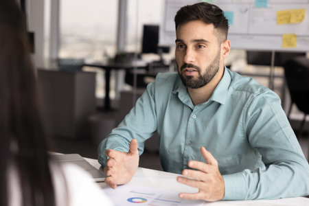 Professional man explains information presented in charts on table, outlining next steps of business strategy or project plan, share idea, point of view to client or colleague during meeting in officeの写真素材