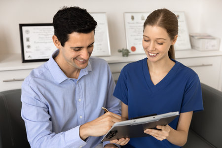 Happy male patient filling hospital application form, writing in medical document with help of...