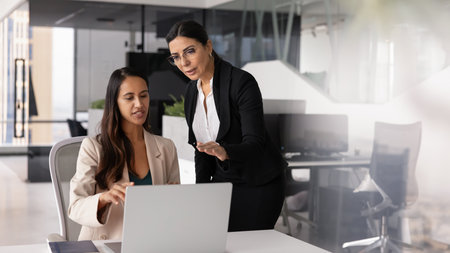 Two different aged female business coworkers meeting at laptop for cooperation, brainstorming on ideas for online product promotion, discussing content, pointing at monitor, talking. Banner shotの写真素材