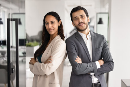 Two diverse young business partners posing for corporate portrait with shoulders touch and hands crossed, looking at camera, smiling. Confident multiethnic couple of managers standing for pictureの写真素材