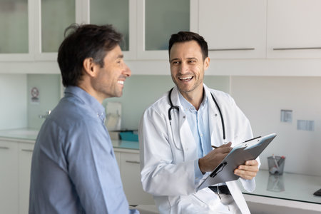 Good news about health. Happy male doctor therapist meet patient in clinic share laughter after examination support visitor in overcoming disease celebrate recovery notice positive treatment dynamicsの写真素材