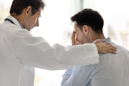 Psychological support in medicine. Understanding doctor hold hand on shoulder of stressed grieving male patient comfort after facing difficult diagnosis encourage strength motivate to fight diseaseの写真素材