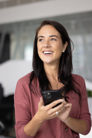 Pensive woman stands in professional workspace with smartphone, busy in task list management,...