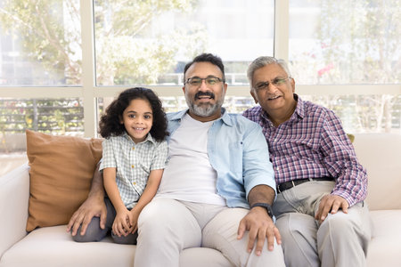 Happy middle aged Indian dad, grandpa and cute positive girl posing for family portrait at home,...