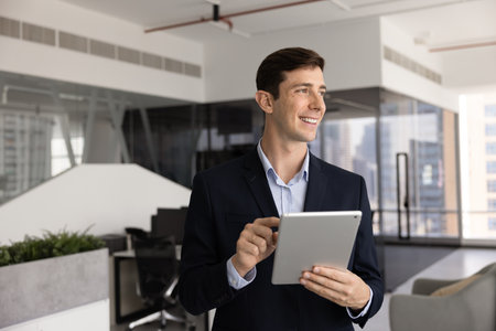 Happy ambitious young online project manager man using tablet in office, holding digital device,...