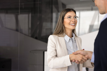 Happy confident Latin business leader woman in stylish glasses shaking hands with male cooperation partner, colleague, closing deal, giving greeting handshake to coworker manの写真素材