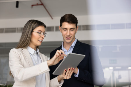 Female professional expert woman explaining electronic document to male coworker, showing tablet pc, speaking, typing on gadget. Coworkers using digital device for teamworkの写真素材