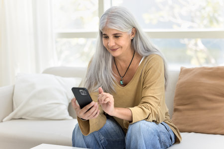Happy senior Hispanic woman chatting on mobile phone, using web service, ecommerce application at...