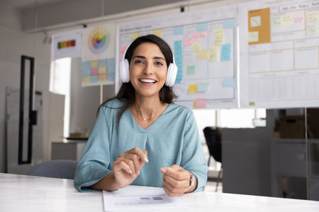 Cheerful beautiful Latin project manager woman wearing headphone talking on online video conference call, looking and speaking at camera with toothy smile. Screen head shot portraitの写真素材