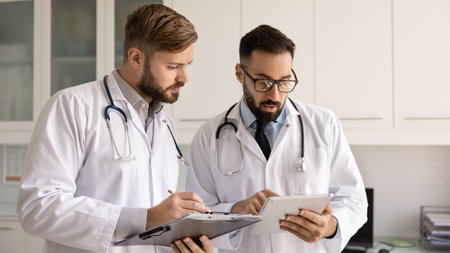 Two multiethnic focused general practitioners engaged in medical case study in clinic office, reviewing patient history, discussing treatment option, learning new e-health app or platform in workplaceの写真素材