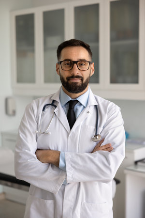 Portrait of medical specialist, GP doctor in coat posing for camera at workplace with arms crossed, smiling, feel satisfied with career, looks confident, strands in clinic office. Mission, healthcareの写真素材
