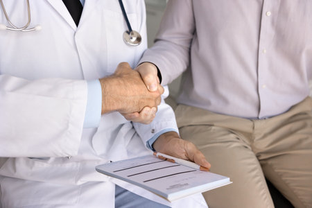 Close up image of male doctor dressed in white coat holds notepad and shaking hands with man...