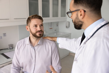 Man therapist or cardiologist puts his hand on male patient shoulder, lead conversation about further operation, treatment plan or diagnose, reassuring, provides professional healthcare consultationの写真素材