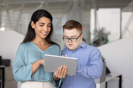 Happy advisor woman giving professional support to young employee, showing online content on tablet...