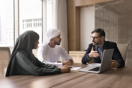 Good investment. Confident businessman professional insurer real estate broker financial advisor consult Arab couple offer insurance policy explain contract details show portfolio on notebook screenの写真素材