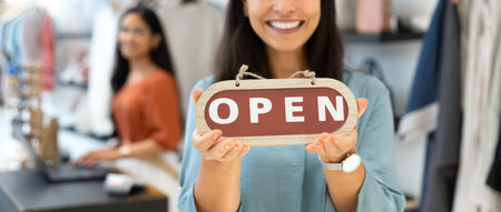 Friendly young small business owner woman holding Open sign, welcoming in fashion shop, smiling at...