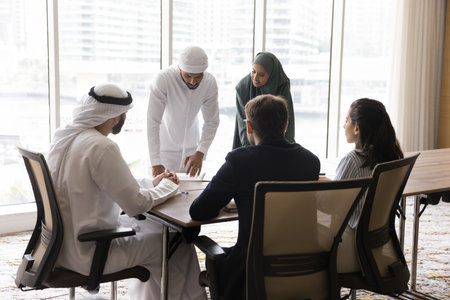Successful teamwork. Young multicultural corporate business team of diverse ethnicities meet by table in conference room review work on project discuss paperwork share ideas collaborate brainstormingの写真素材
