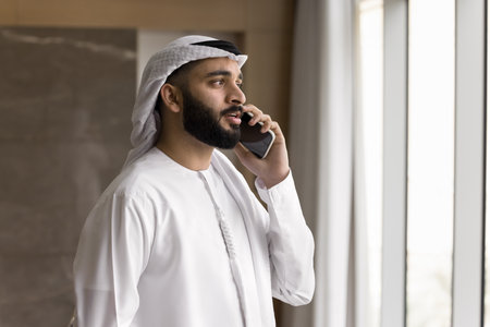 Serious phone talk. Busy young Arab man in dishdasha business leader speak on cell give instructions to employee support client with professional legal advice discuss deal terms conditions. Copy spaceの写真素材