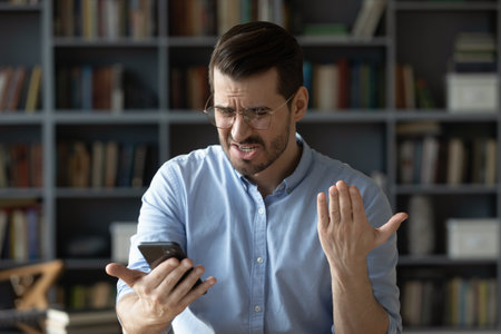 Bad news in message. Nervous angry young adult businessman remote working employee stressed reading...