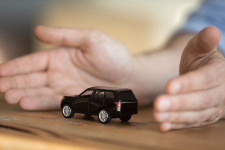 Best solutions for your car. Close up male hands protect toy crossover model on desk. Professional assistance in buying selling automobile auto market service loan insurance rental dealership conceptの写真素材
