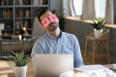 Funny procrastination. Lazy unmotivated millennial businessman office employee sleep at workplace hold comic sticky notes with wide open eyes on face simulating work delaying boring stressful tasksの写真素材