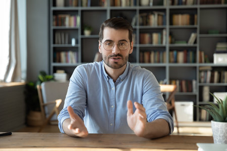 Webcam communication. Screen view portrait confident young male teacher expert coach sit at desk speak talk online lead webinar tutorial stream live training lesson via videocall virtual conferenceの写真素材