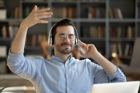 Conducting imaginary orchestra. Carefree mindful young male freelancer office worker in wireless...