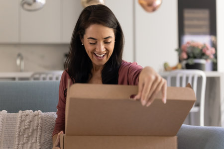 Happy excited Hispanic customer woman opening logistic cardboard box at home, unpacking awaited...