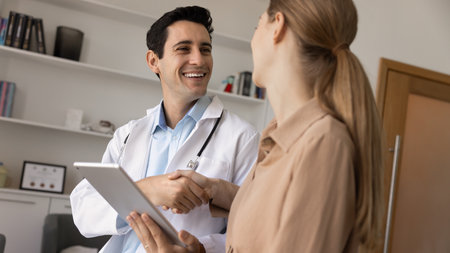 Smiling male doctor in white coat shakes hands with female patient after successful medical consultation in modern clinic, express trust and satisfaction, finalize professional appointment at hospitalの写真素材