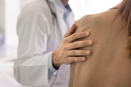 Close up male doctors hand gently resting on female patients shoulder, symbolizing empathy and psychological support during sensitive or difficult conversation about disease news or further operationの写真素材