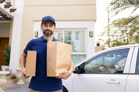 Your order is delivered on time. Confident male courier in uniform stand by car in private residence yard hold packages with online purchases look at camera. Client trust safe reliable service conceptの写真素材
