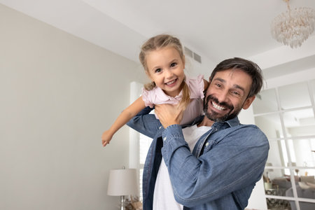 Flying with support of dad. Portrait cheerful happy mature father lifting overjoyed playful toddler daughter in air hold little girl on shoulder in flight pose both laugh looking at camera. Copy spaceの写真素材