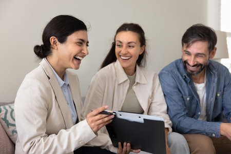Laughter therapy. Laughing female psychologist show paper clipboard to overjoyed family couple patients sharing funny test results using comic sketch as communication tool on relationship consultationの写真素材