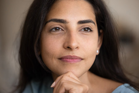 Close up facial portrait of young Latin woman touching chin, face, looking away, smiling in deep...