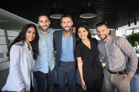 Business team unity in workplace. Diverse multiracial smiling corporate staff workers employees unite in group posing for portrait embracing looking at camera feeling spirit of teamwork collaborationの写真素材