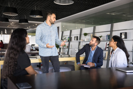 Presenting idea. Inspired young man professional speaking before engaged multicultural team of diverse colleagues meeting in stylish coworking environment share startup plan propose work innovationsの写真素材