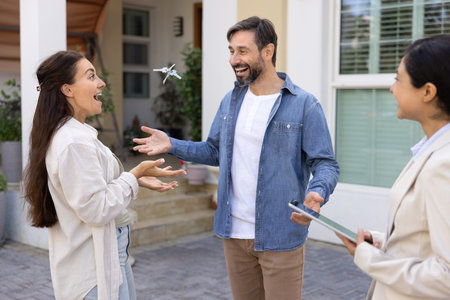 Just closed deal. Excited married couple homeowners celebrate buying house of dream scream laugh have fun toss keys from new home into air after signing sale purchase contract with smiling realtorの写真素材