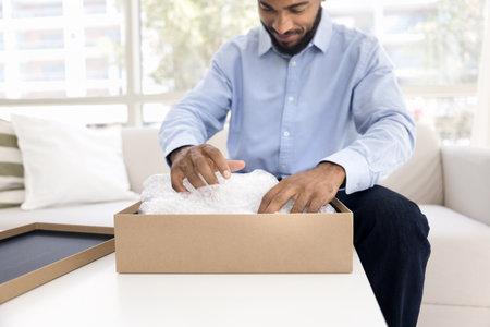 Cropped close up view young man opening cardboard parcel box with received present, smile, enjoy purchased goods through electronic commerce, marketplace platform or webstore. Positive feedback, giftの写真素材