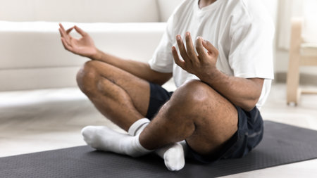 Close up cropped shot African man in activewear meditating seated cross-legged on mat at home, relieving stress, anxiety or fatigue, boost positive energy flow, practicing mindfulness. Yoga, lifestyleの写真素材